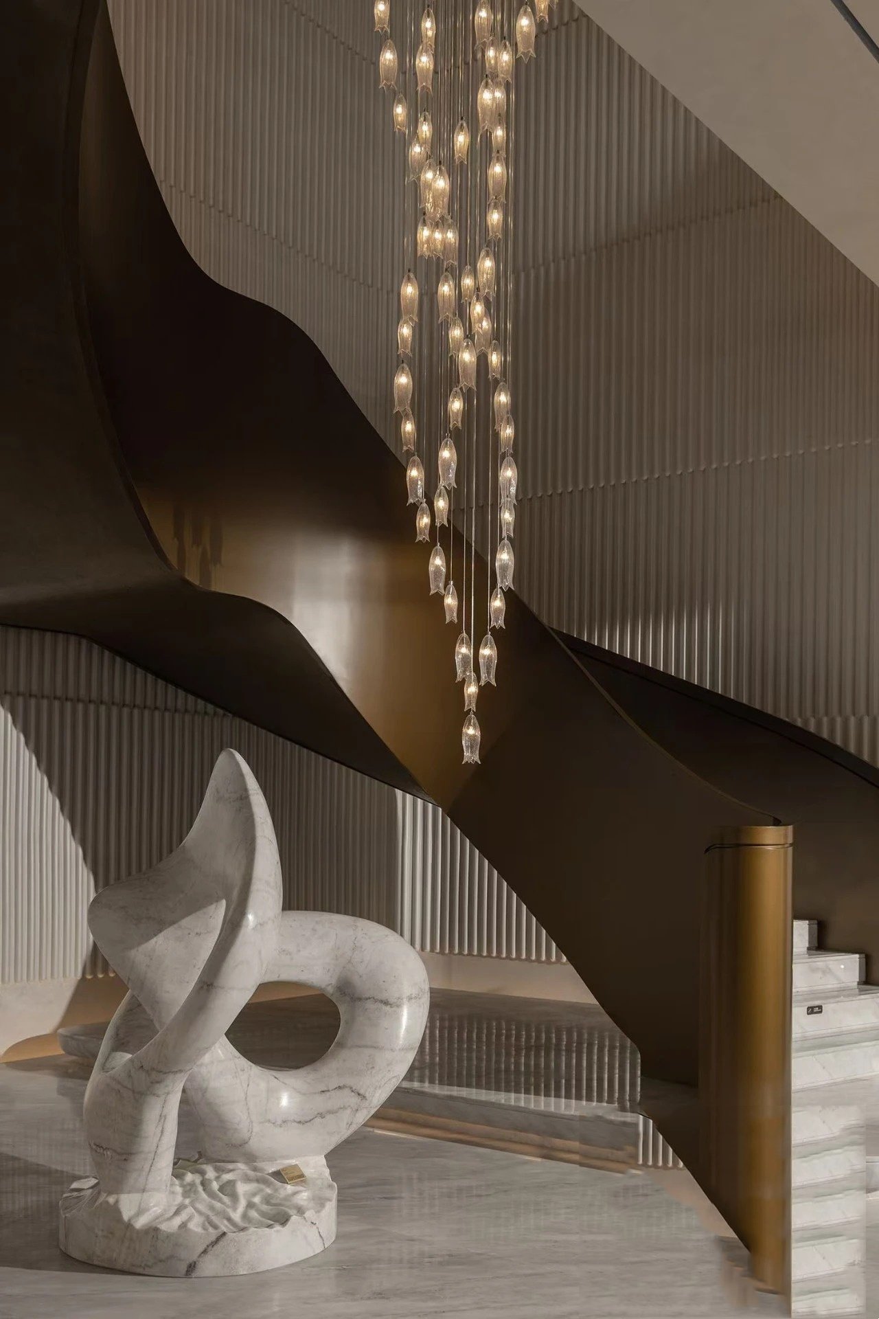 Sculptural helical Architectural Metal Staircase featuring a continuous PVD bronze ribbon stringer and balustrade.