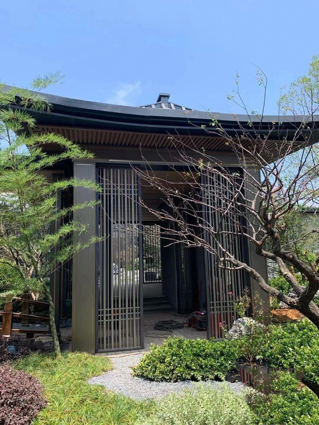 Architectural metal garden pavilion functioning as a landscape gateway with a modern Chinese-style roof and louvered sides.