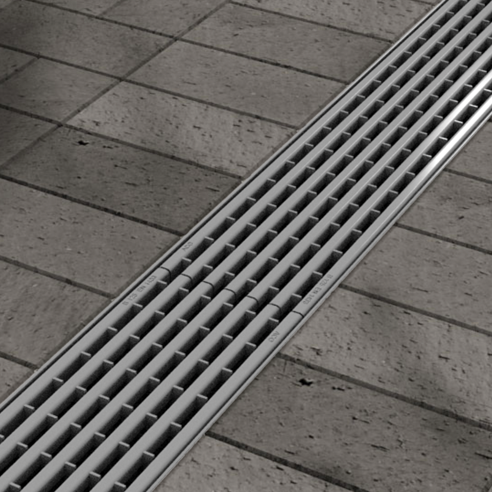 Architectural linear Stainless Steel grating installed in an outdoor walkway with stone pavers, serving as a seamless integrated trench drain system