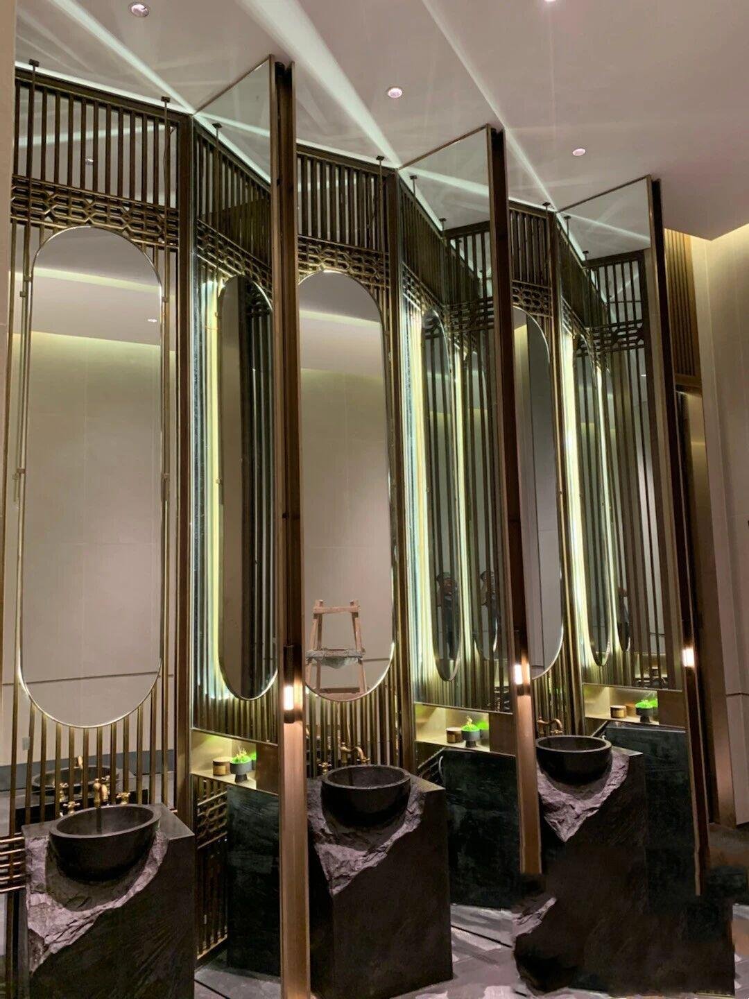 Architectural Metal Partitions featuring backlit ornate metalwork and integrated mirrors for premium washroom and spa environments