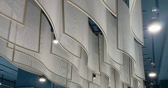 Curved expanded metal mesh panels used for bespoke interior ceiling cladding in a modern public transport hub.