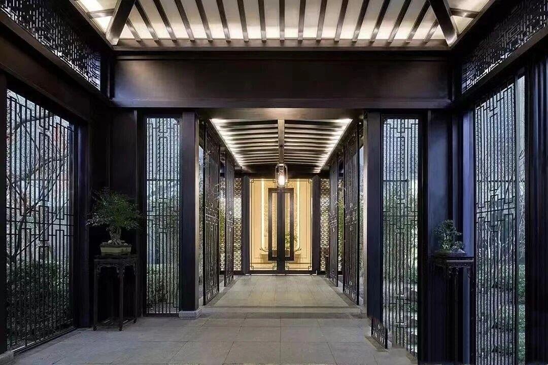 A dark, modern pergola corridor, featuring a louvered ceiling with integrated lighting and decorative metal screens on both sides.