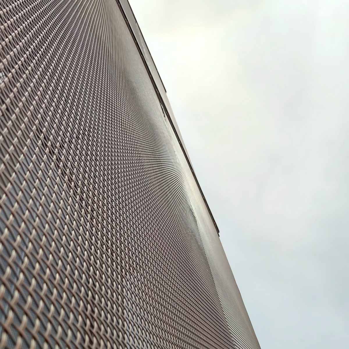 Low-angle view of a bronze-finished architectural woven wire mesh facade, highlighting its geometric aesthetic