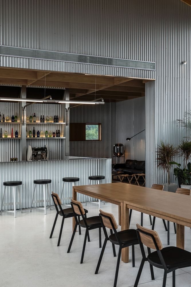 A restaurant interior showcasing galvanized corrugated metal sheets used as both bar front cladding and a bold, industrial wall siding, providing a modern, raw aesthetic.