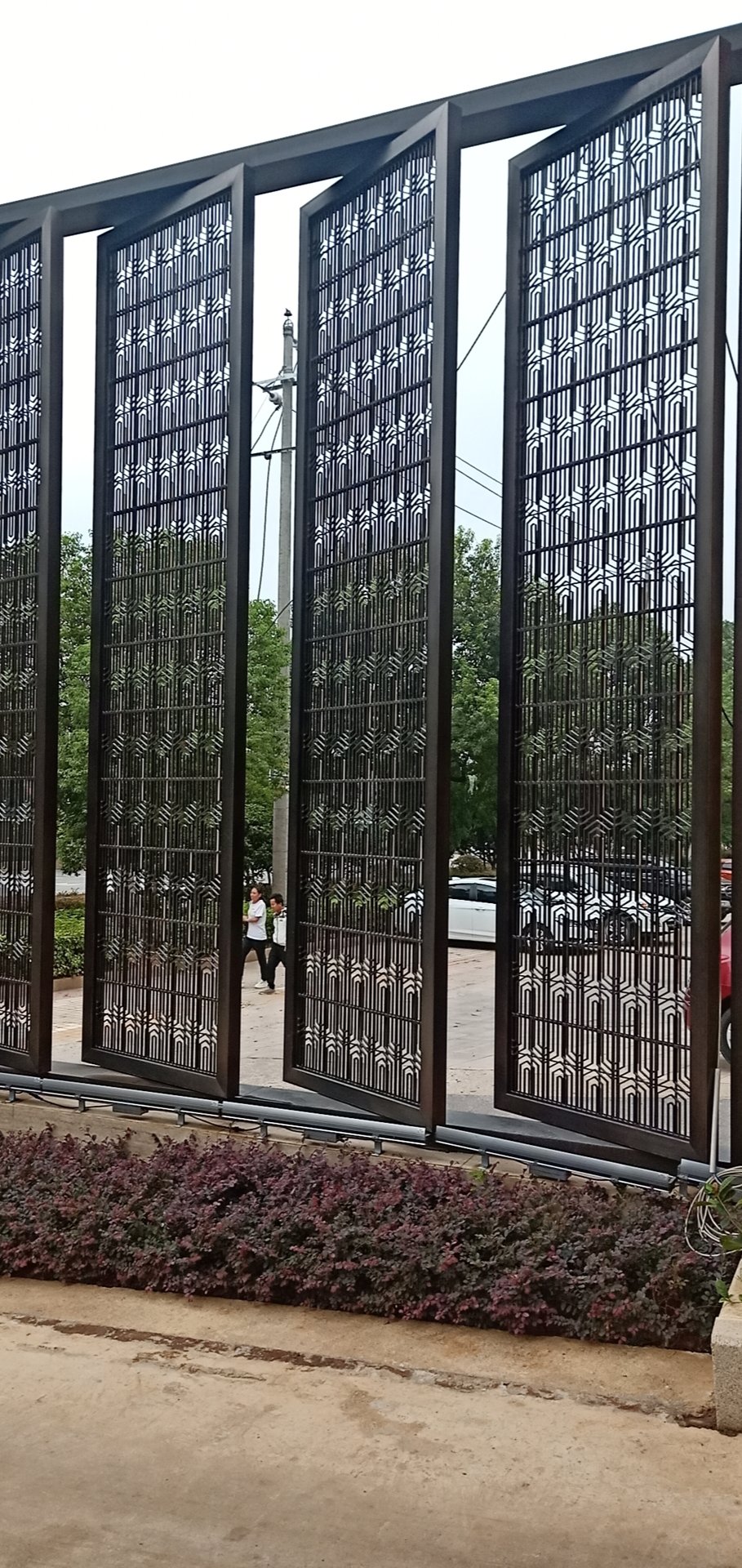 Tall exterior entryway screens made from geometric laser-cut stainless steel sheets for architectural security and privacy.