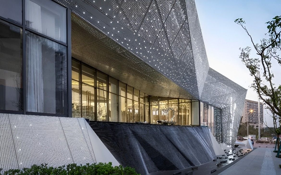 Custom geometric perforated stainless steel facade system for a luxury commercial building featuring integrated night lighting.