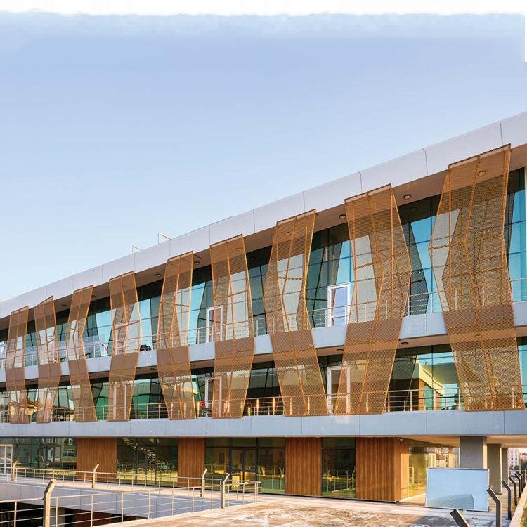 Gold anodized aluminum mesh facade featuring custom-fabricated sunshade screens for hospitality building energy efficiency.