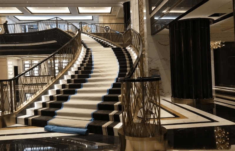Ornate gold-finished decorative lattice balustrade for a grand winding staircase in a luxury hotel lobby.