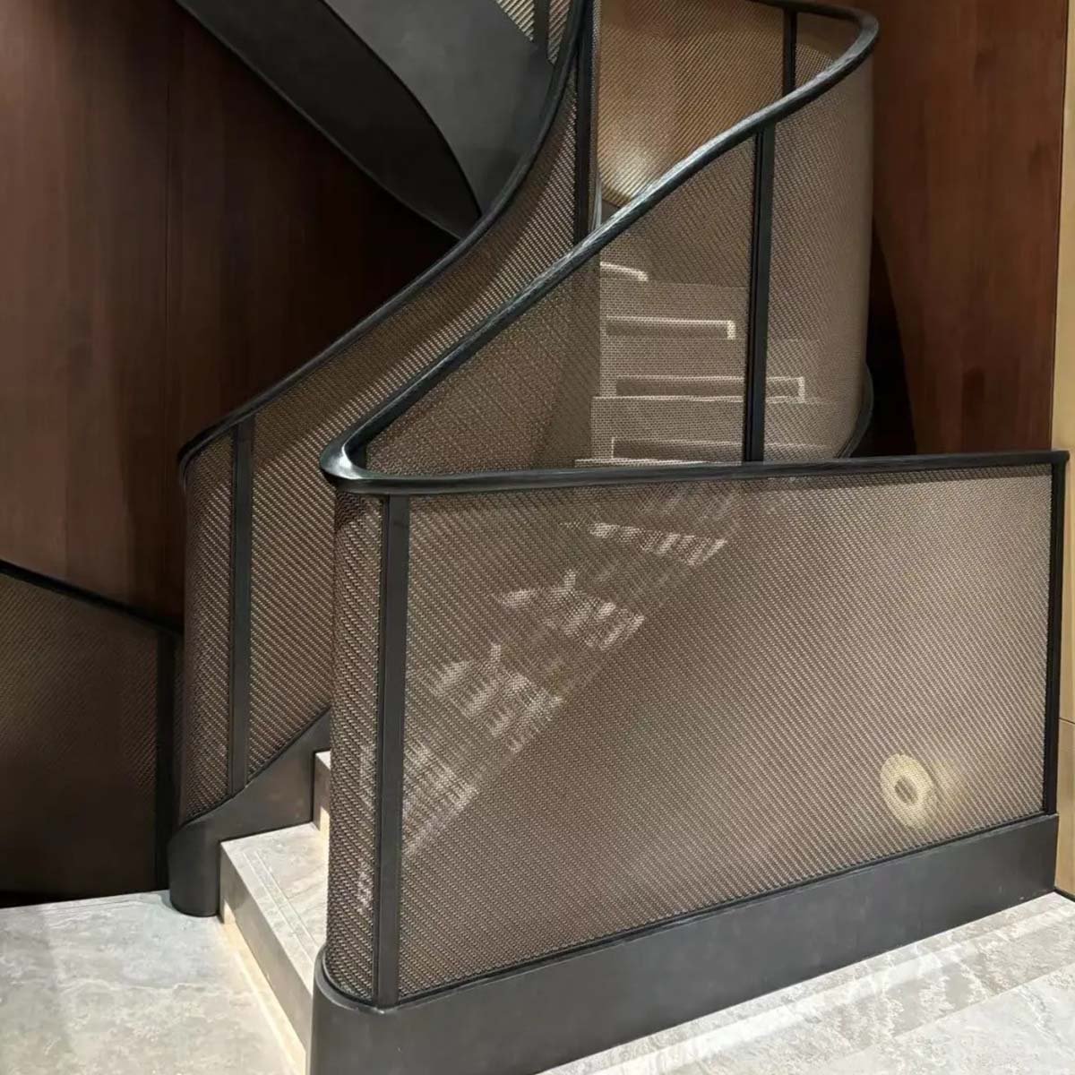 Dark-finished woven wire mesh installed on a spiral staircase as a secure and stylish balustrade panel