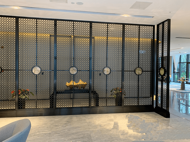 Custom black laser-cut stainless steel sheets used as functional and artistic interior screen dividers in a luxury hotel lobby.