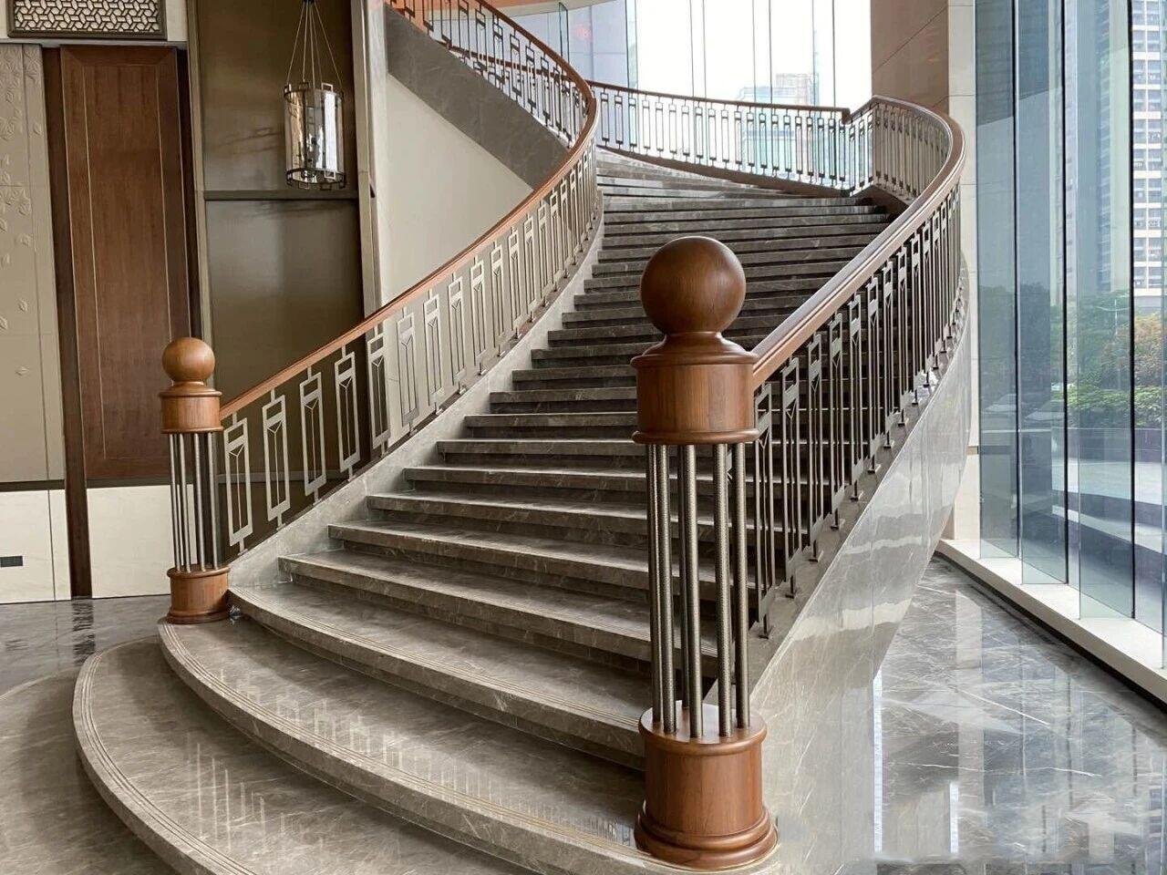 High-end curved marble staircase featuring a custom metal balustrade with an integrated wood top rail for hospitality interiors.