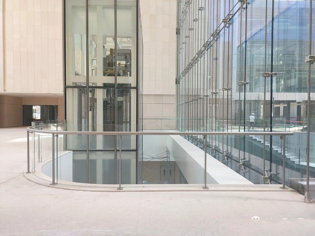 Stainless Steel Railing Systems and Architectural Balustrades featuring a minimalist curved glass design for a luxury commercial atrium with a glass elevator.