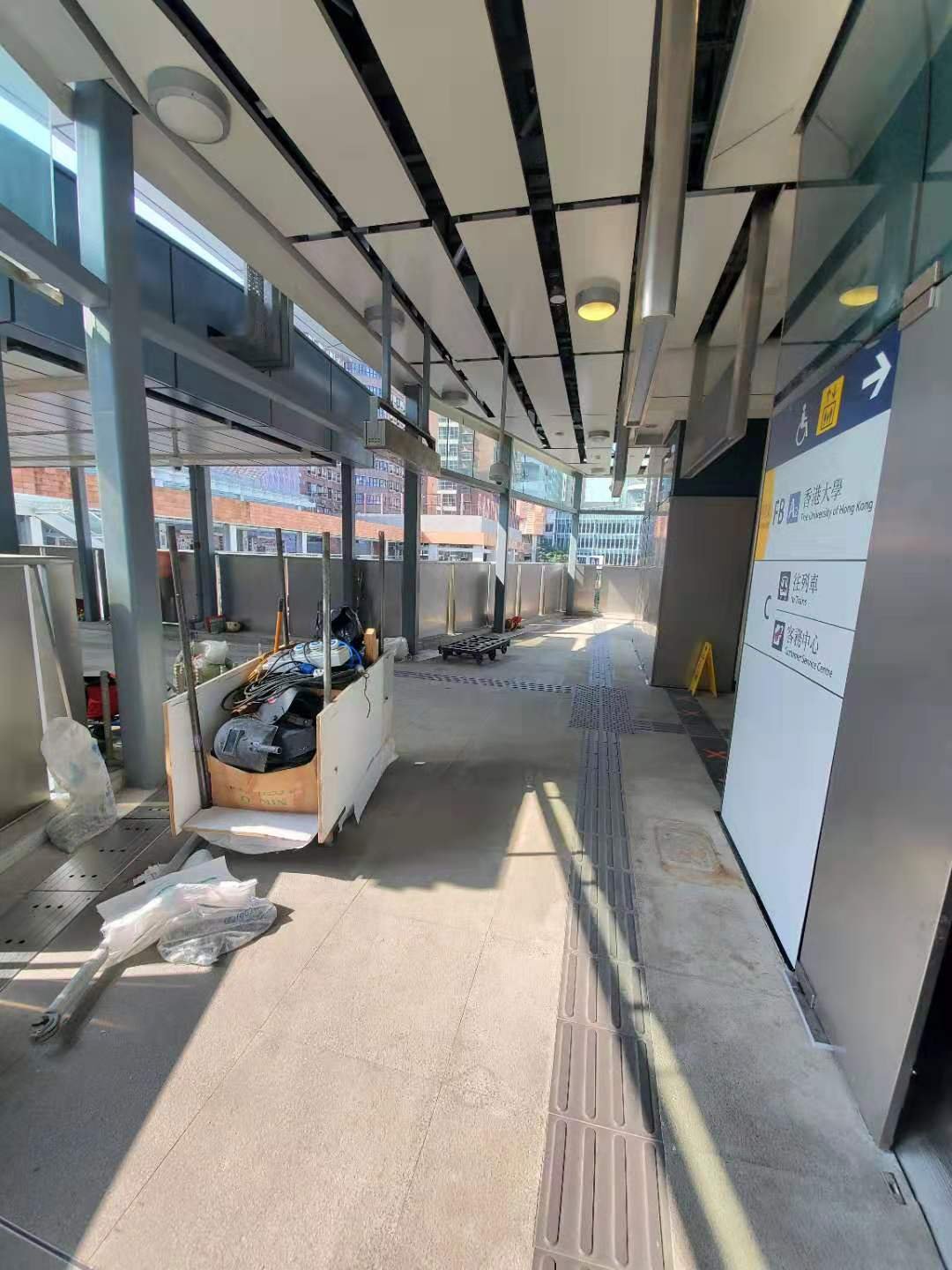 A modern, functional pergola in a public transport station, featuring a high ceiling with white metal baffles (louvers) for shading.