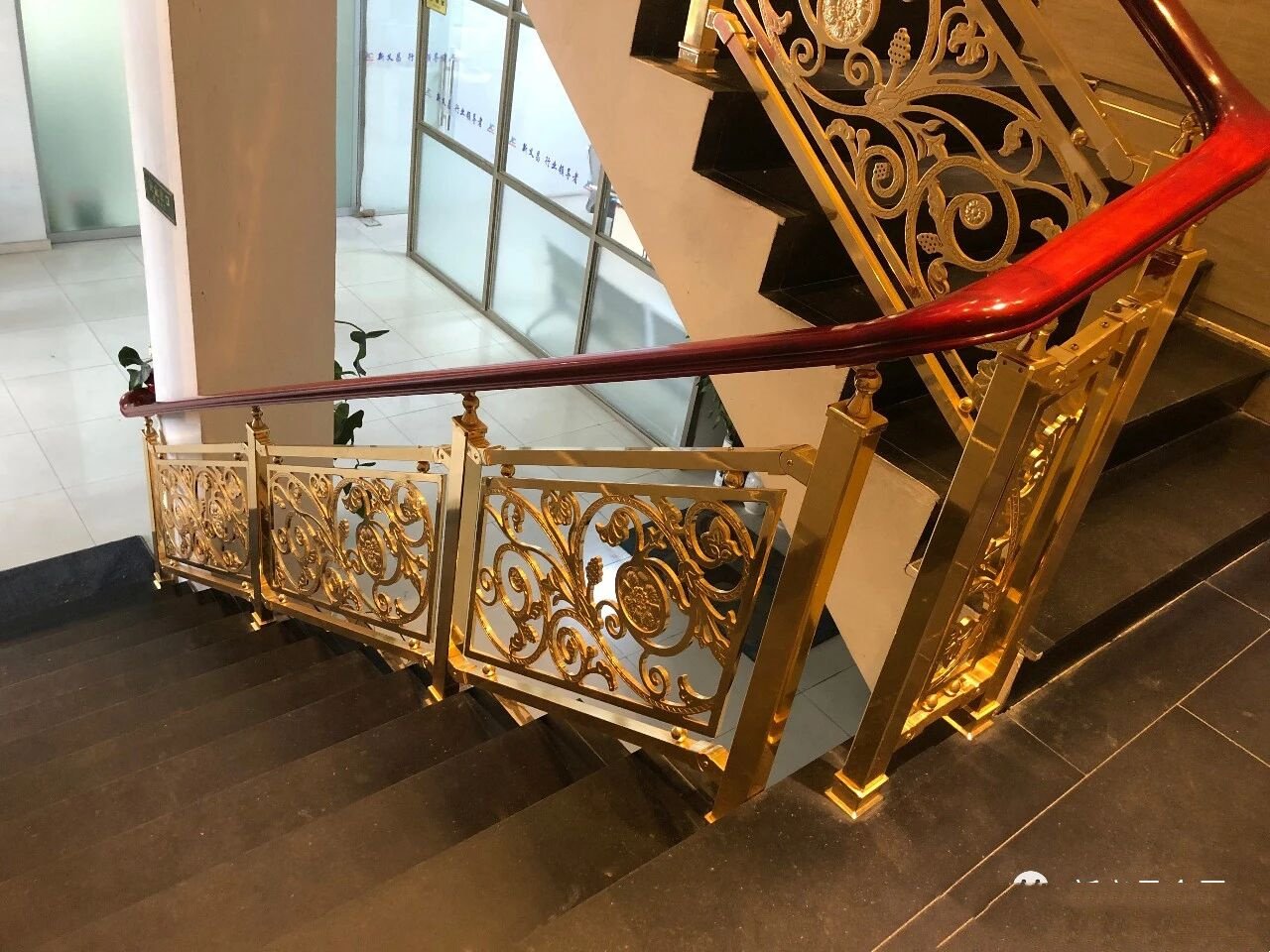 Highly decorative gold-finished scrollwork stair balustrade with a contrasting mahogany wood top rail.