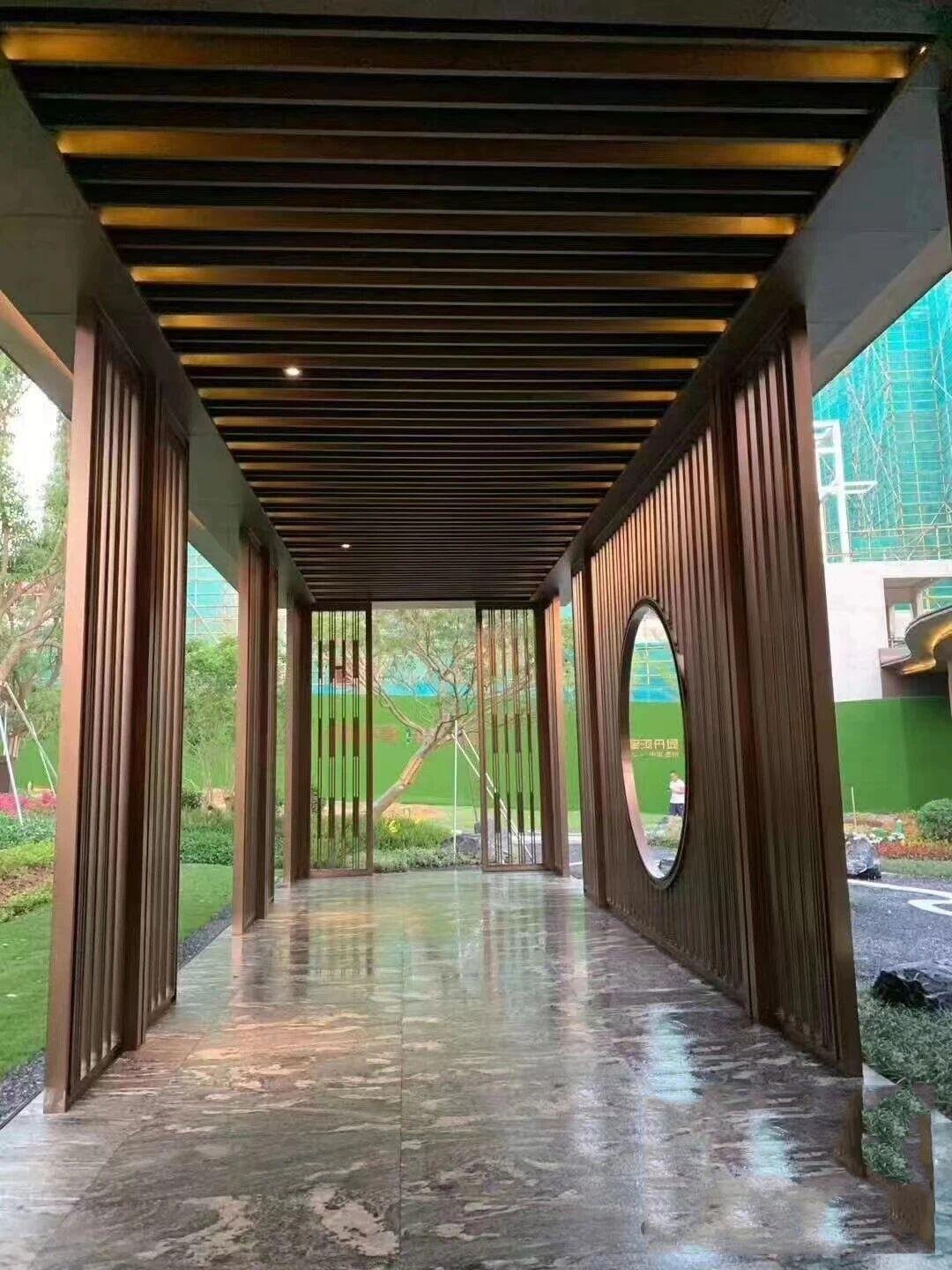 A modern pergola corridor fabricated from sandblasted antique bronze stainless steel, featuring a louvered ceiling and a circular 'moon gate' wall