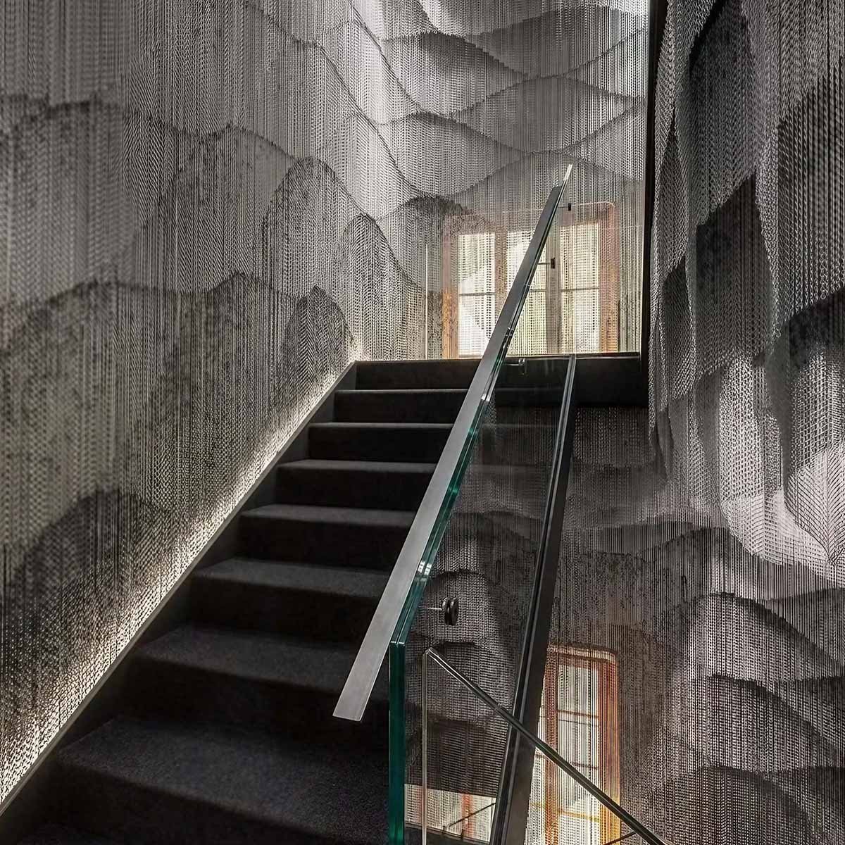 Wavy architectural woven wire mesh installation creating a semi-transparent feature wall in a modern stairwell