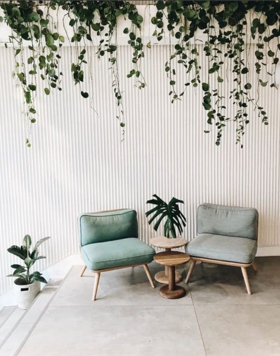 A bright, modern interior featuring a white powder-coated corrugated metal sheet as a feature wall, elegantly contrasting with green plants and soft furnishings.