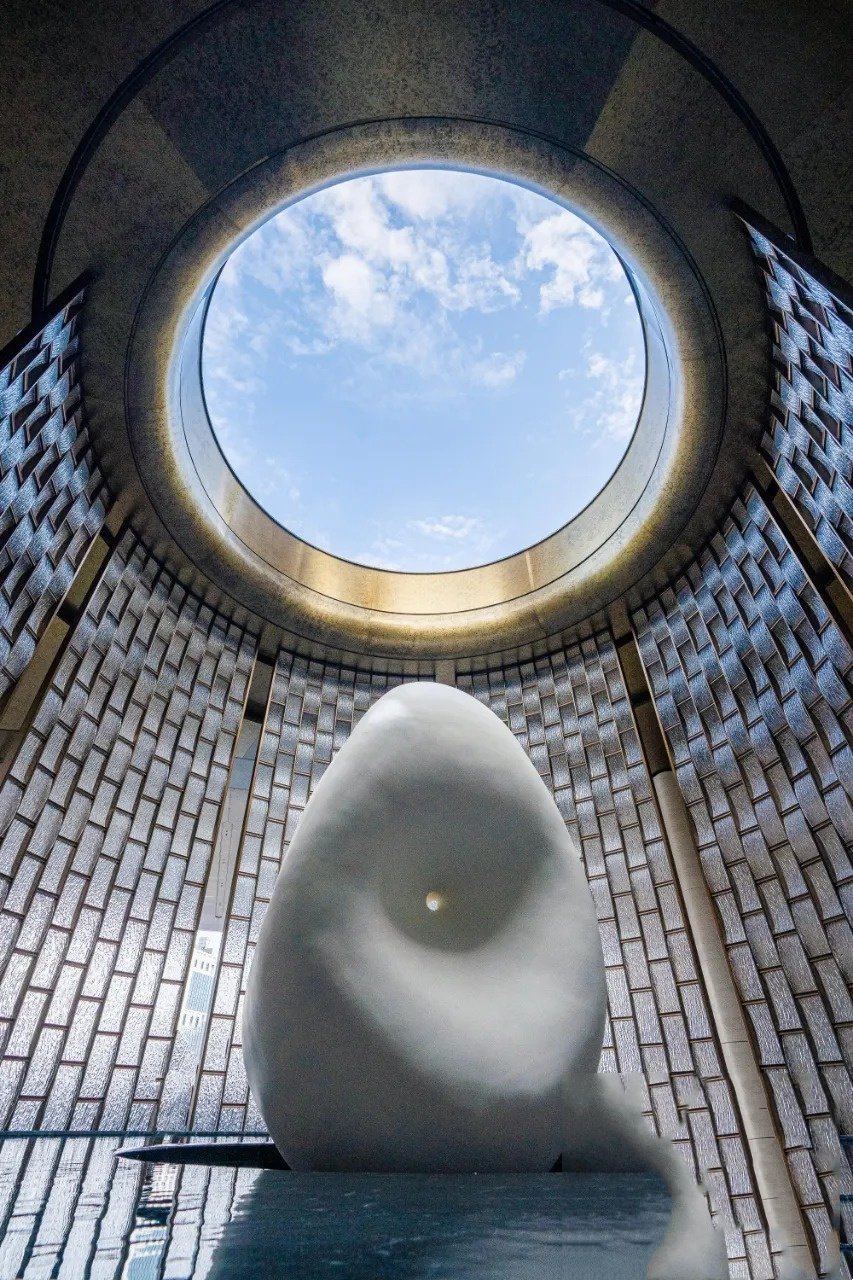 Modern smooth abstract sculpture under a circular skylight oculus for interior architectural art by XYC Metalworks.
