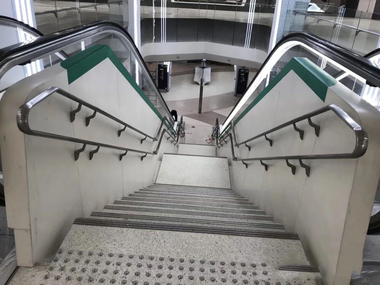 Wall-mounted double-height stainless steel safety handrails for exterior public stairs in high-traffic transportation or commercial areas.