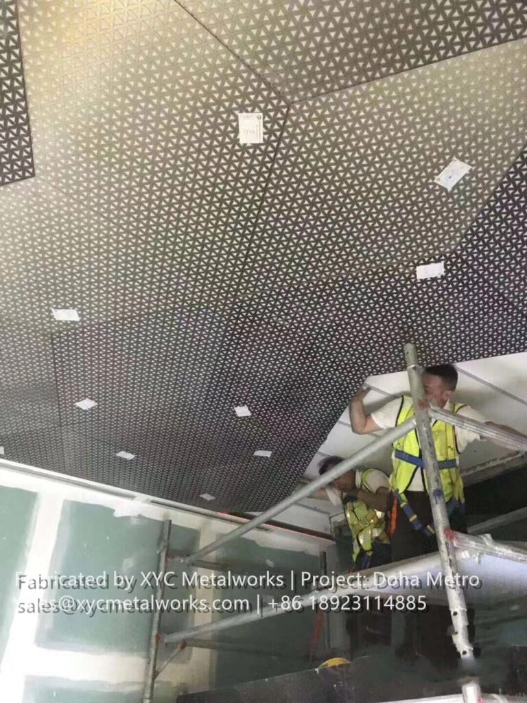 Skilled workers installing complex geometric metal ceiling panels at a Doha Metro station construction site.