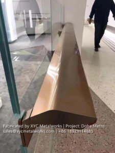 Close-up of a custom-profile bronze handrail on glass balustrade for Doha Metro, precision-engineered by XYC METALWORKS.