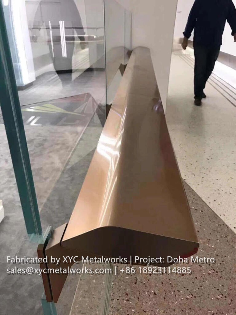 Close-up of a custom-profile bronze handrail on glass balustrade for Doha Metro, precision-engineered by XYC METALWORKS.
