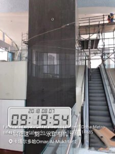 A large-scale perforated metal mesh pillar cover by XYC Metalworks installed near a Doha Metro escalator, dated August 2018 in Qatar.