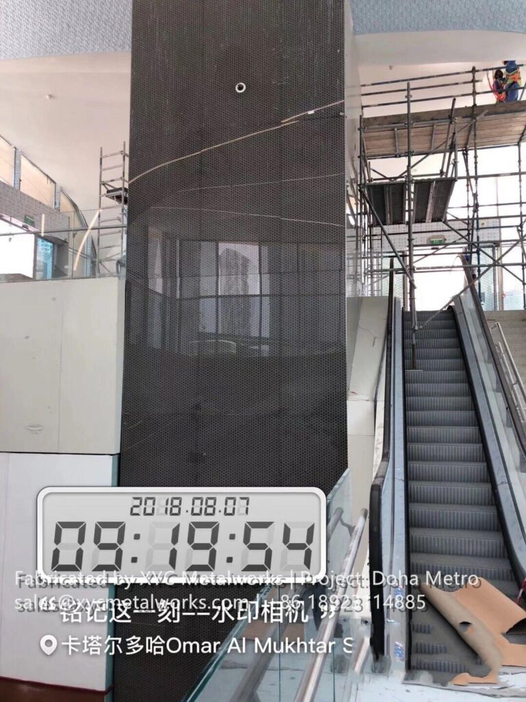 A large-scale perforated metal mesh pillar cover by XYC Metalworks installed near a Doha Metro escalator, dated August 2018 in Qatar.