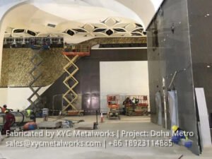 A wide shot of a Doha Metro station under construction featuring scissor lifts and workers installing custom architectural wall cladding by XYC Metalworks.